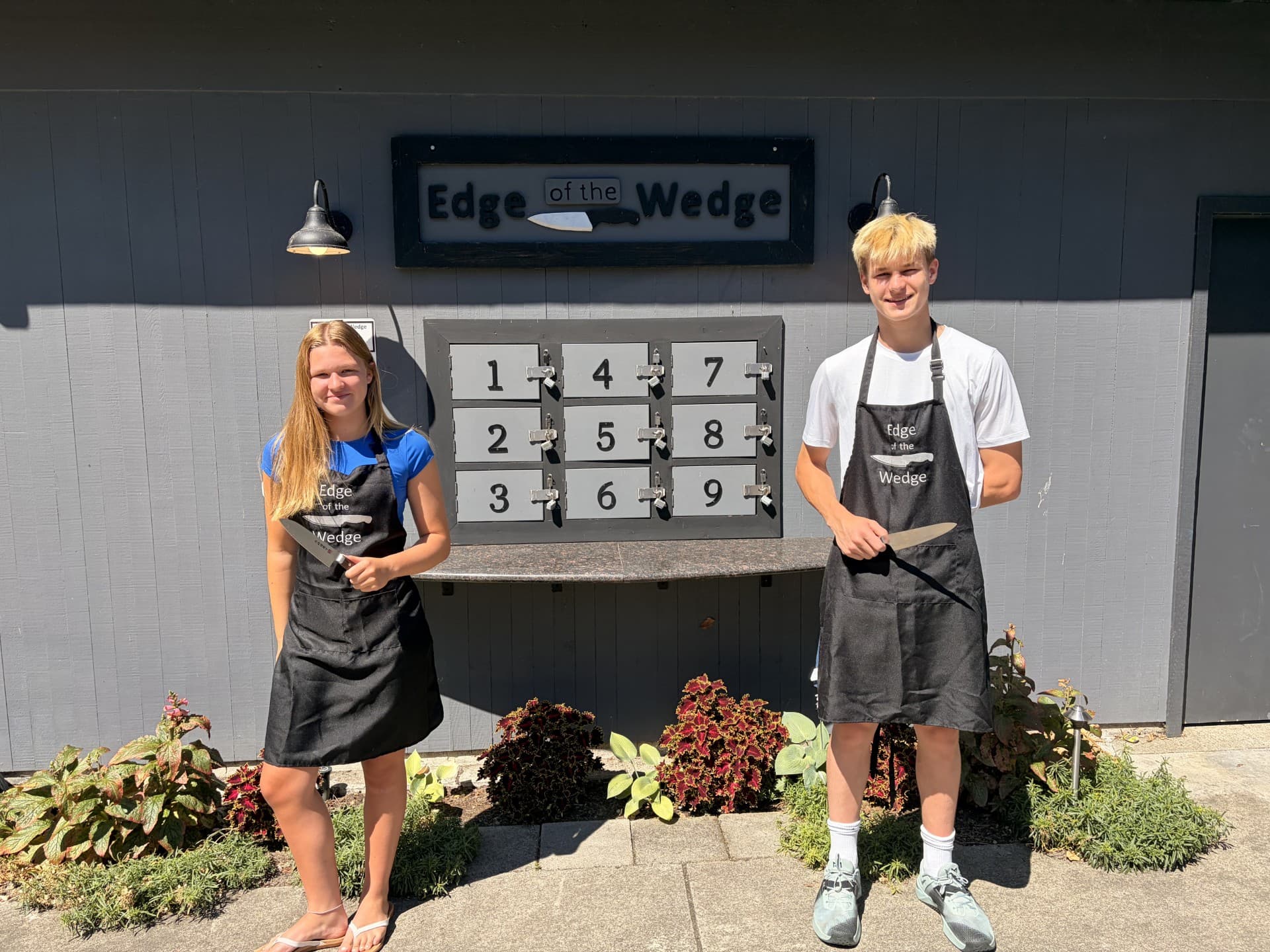 Dash and Clara wearing Edge of the Wedge aprons beside the secure knife drop-off lockers